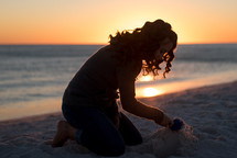 a woman building a sandcastle in the sand at sunset 