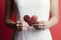 A woman in a white dress holding a paper heart 