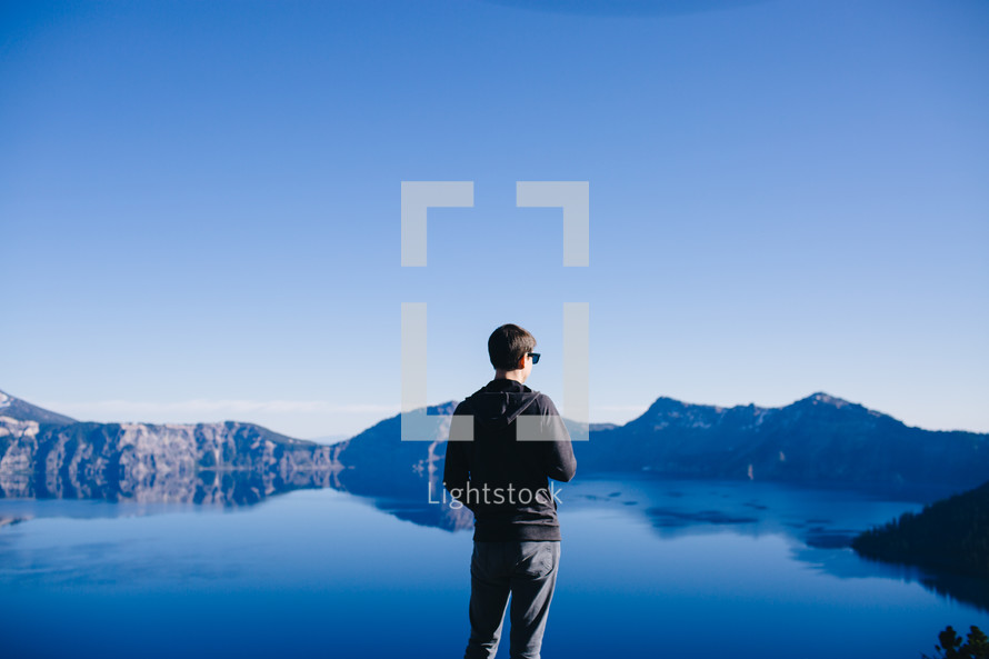 man standing in front of a mountain lake