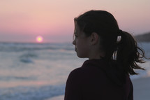 a girl looking out at the ocean at sunset 