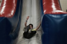 a boy sliding down a bouncy house slide at a carnival 
