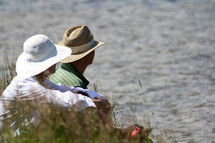 husband and wife sitting on a beach wearing hats 