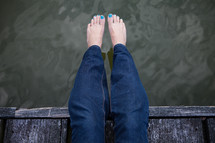bare feet with painted toenails hanging over water 