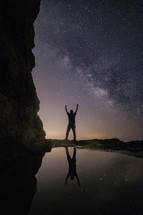 man with raised arms standing under a starry night sky 