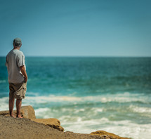 man standing on a shore looking out at the water 