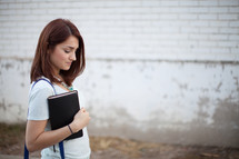a young woman walking carrying a Bible 