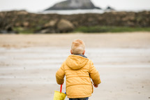 toddler boy in a coat playing on a beach 