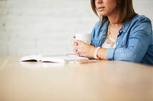 a woman holding a coffee mug and reading a Bible 