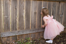 toddler girl peeking through gaps in a fence 