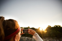 a woman taking a picture of the sunset with her cellphone 