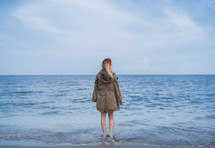 a girl in a coat standing in the ocean 