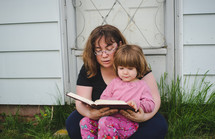 mother and daughter reading a Bible together outdoors