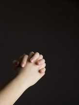 praying hands against a black background 