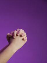 praying hands against a purple background 