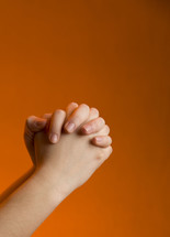 praying hands against an orange background 