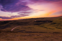 rural road over hills and purple sky at sunset 