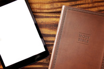 tablet and Bible on a wood desk 