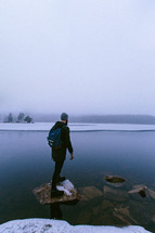 Man standing on a rock at the edge of an icy lake