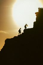 silhouettes of fishermen walking up a slope at sunset 