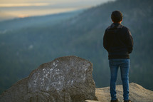 a man standing on a mountaintop looking out at the view 