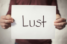 a man holding a piece of paper with the word lust on it 