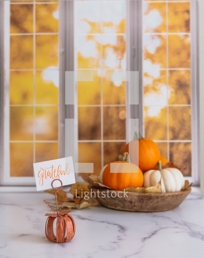 Orange and white pumpkins with a grateful sign in front of autumn window