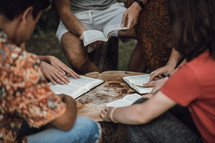 adult Bible study outdoors around a tree stump 