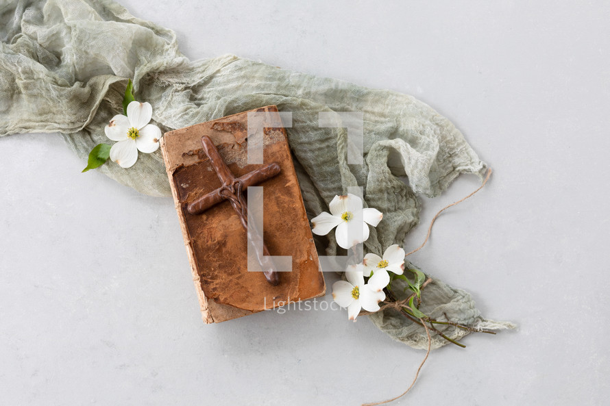 wooden cross on an old Bible and dogwood flowers 