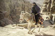 Woman riding a donkey up rocky hills