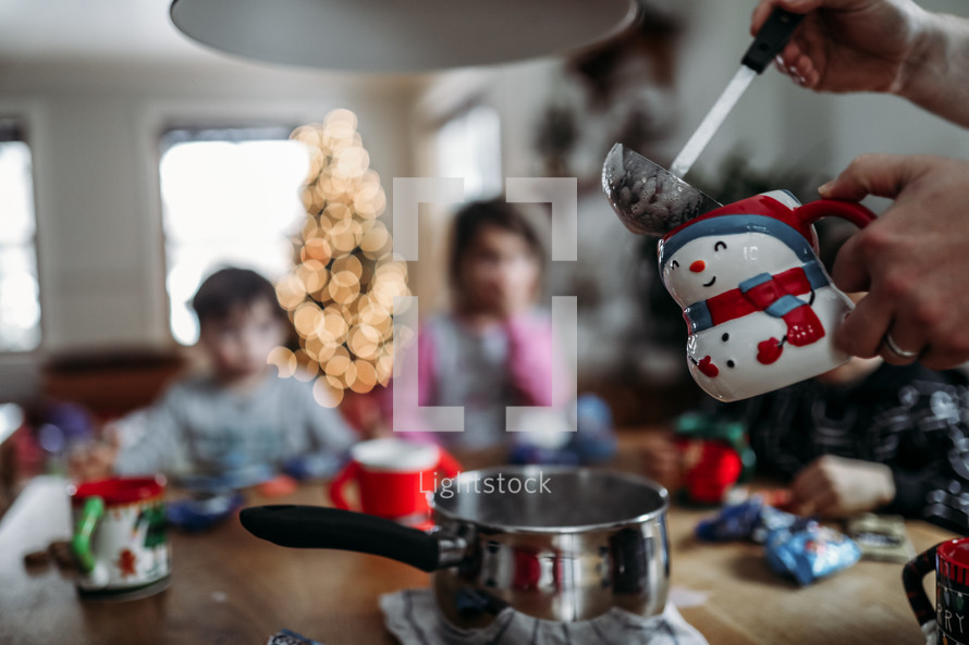 father pouring hot cocoa into mugs for kids at Christmas 