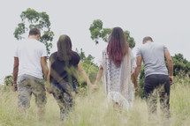 friends walking holding hands through a field of tall grasses 