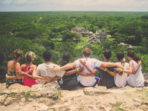 view of ruins as friends sit with arms around each other on a mountain 