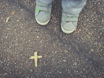 toddler feet and a wooden cross on asphalt 