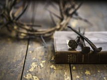 crown of thorns, three nails, and Holy Bible on a wood background 
