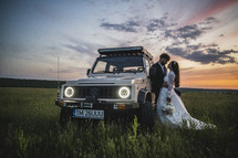 bride and groom near an SUV in a field 