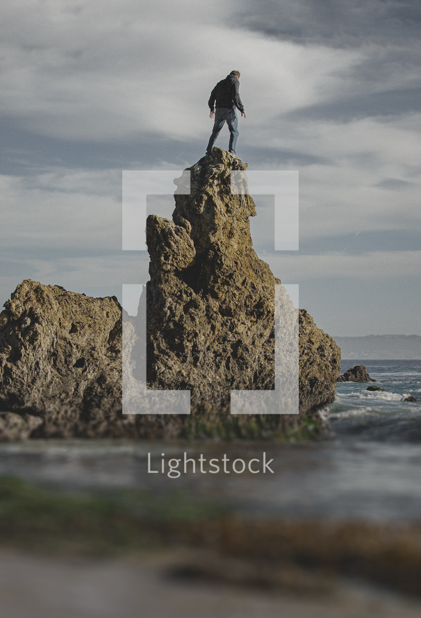 man standing on a steep rock on a shore 