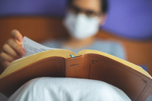 a woman wearing a face mask reading a Bible 