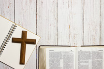 wood cross, notebook, and open Bible on a wood background 