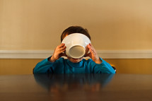 a boy drinking milk out of a cereal bowl 