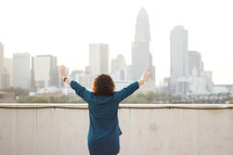 a woman with her back to the camera with raised hands in a city 