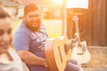 man sitting in a chair outdoors holding a guitar 
