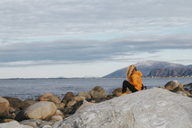 a woman sitting along a rocky shore 