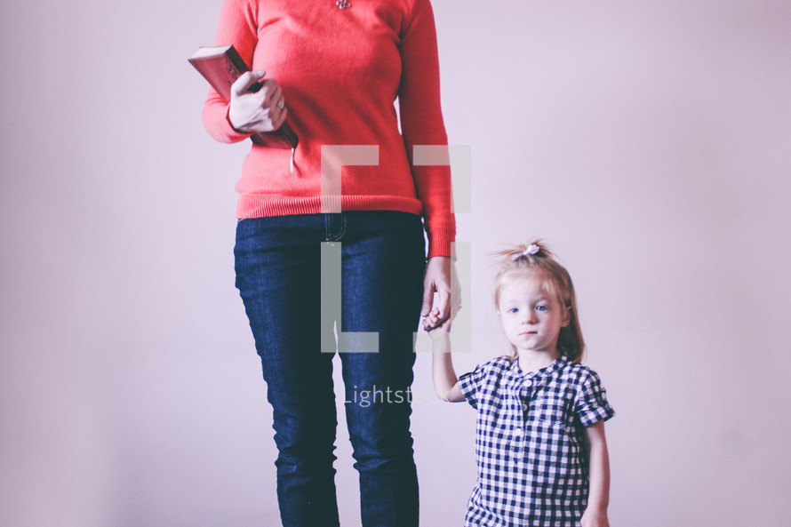 Mother holding a Bible and her daughter's hand.