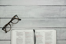 open Bible and reading glasses on gray wood boards 