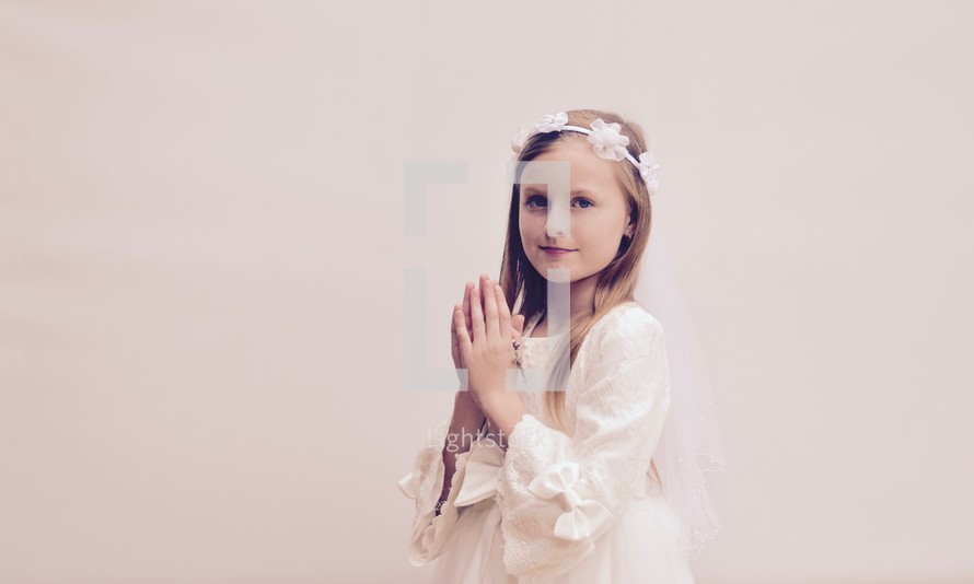 A little girl with praying hands holding a rosary for her First Communion 