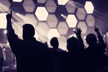 silhouttes of raised hands at a concert 