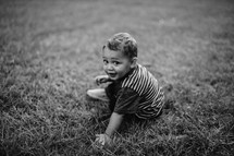a toddler boy sitting in the grass 