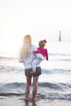 a woman standing in the ocean holding her toddler daughter 