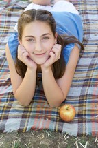 a smiling teen girl lying on a plaid blanket 