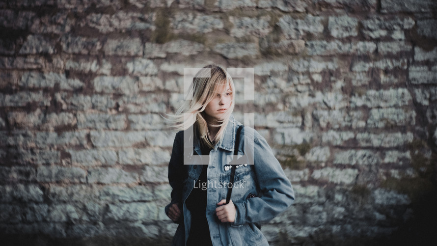 a teen girl walking outdoors in a denim jacket 